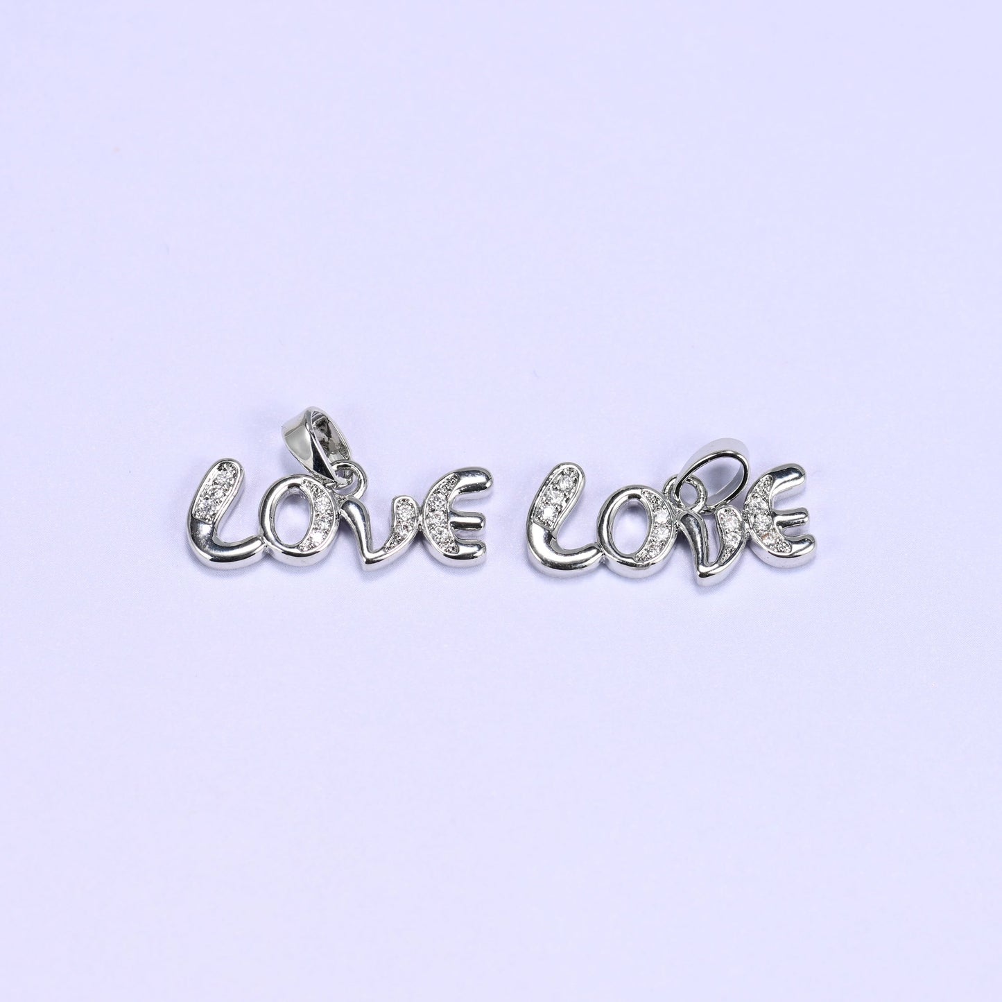 Two silver-tone Love letter zirconia charms lying side by side, the cursive Love script lined with small clear pave stones.