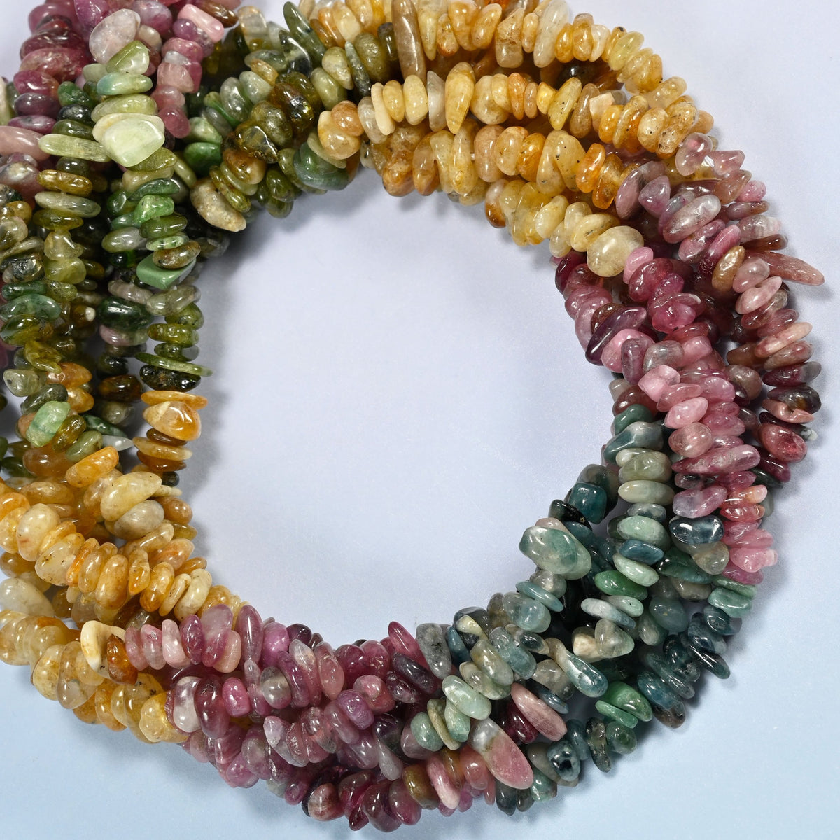 Multicolor tourmaline chip beads coiled into overlapping loops, whole strands of pink, green and golden yellow stone