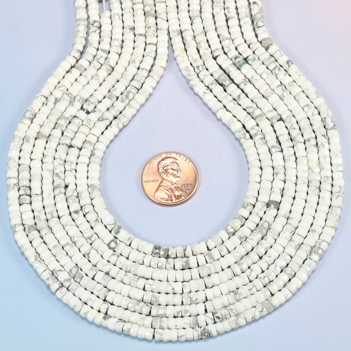 White howlite faceted heishi disc strands formed into a teardrop loop around a US penny for scale