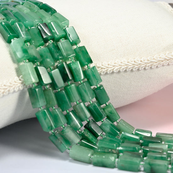 African jade faceted tube beads 7x11-7x12mm with small light green seed bead spacers, several strands draped over a white cushion
