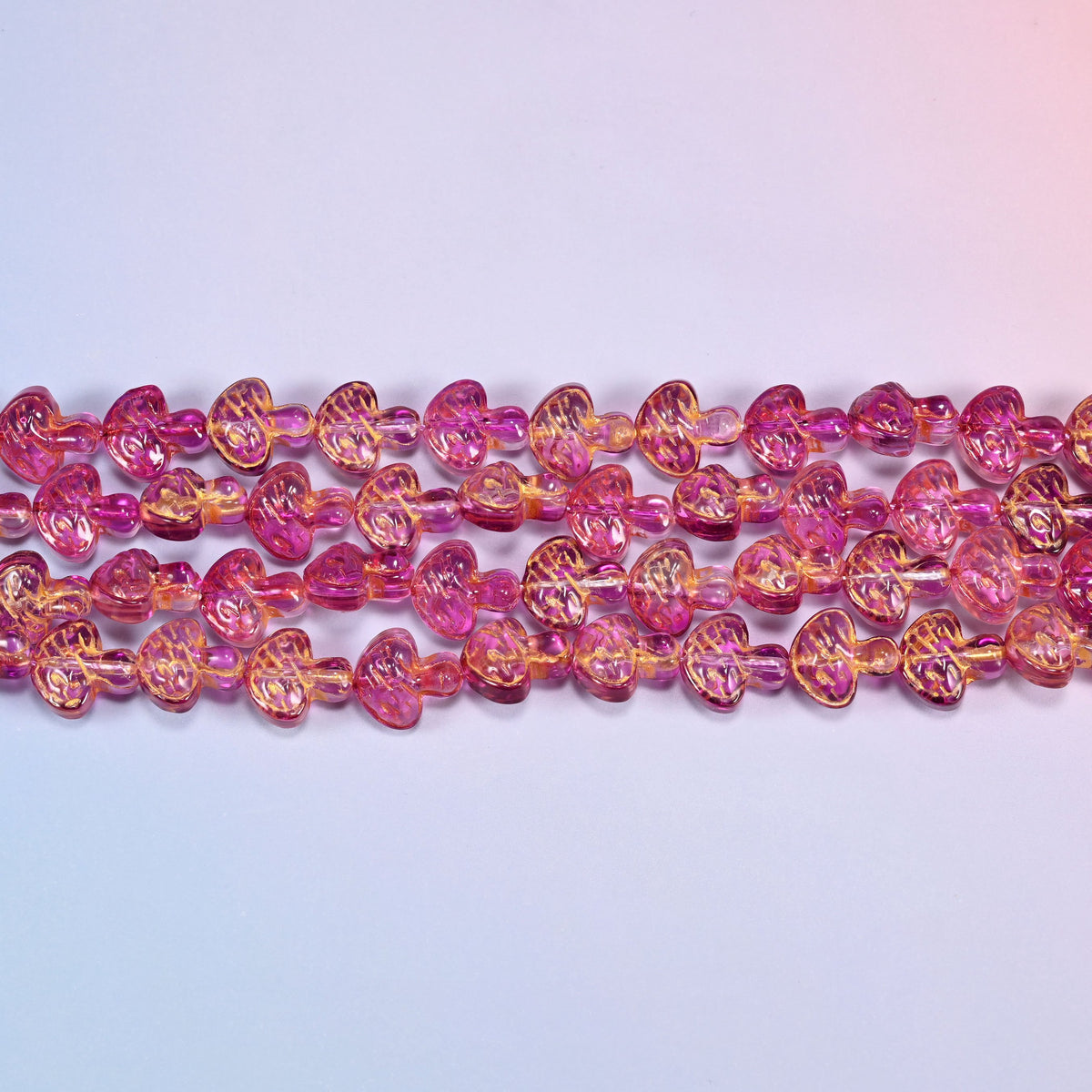 Close-up of 13x12mm pink gold flat mushroom glass beads in four horizontal rows, showing the molded gill lines.
