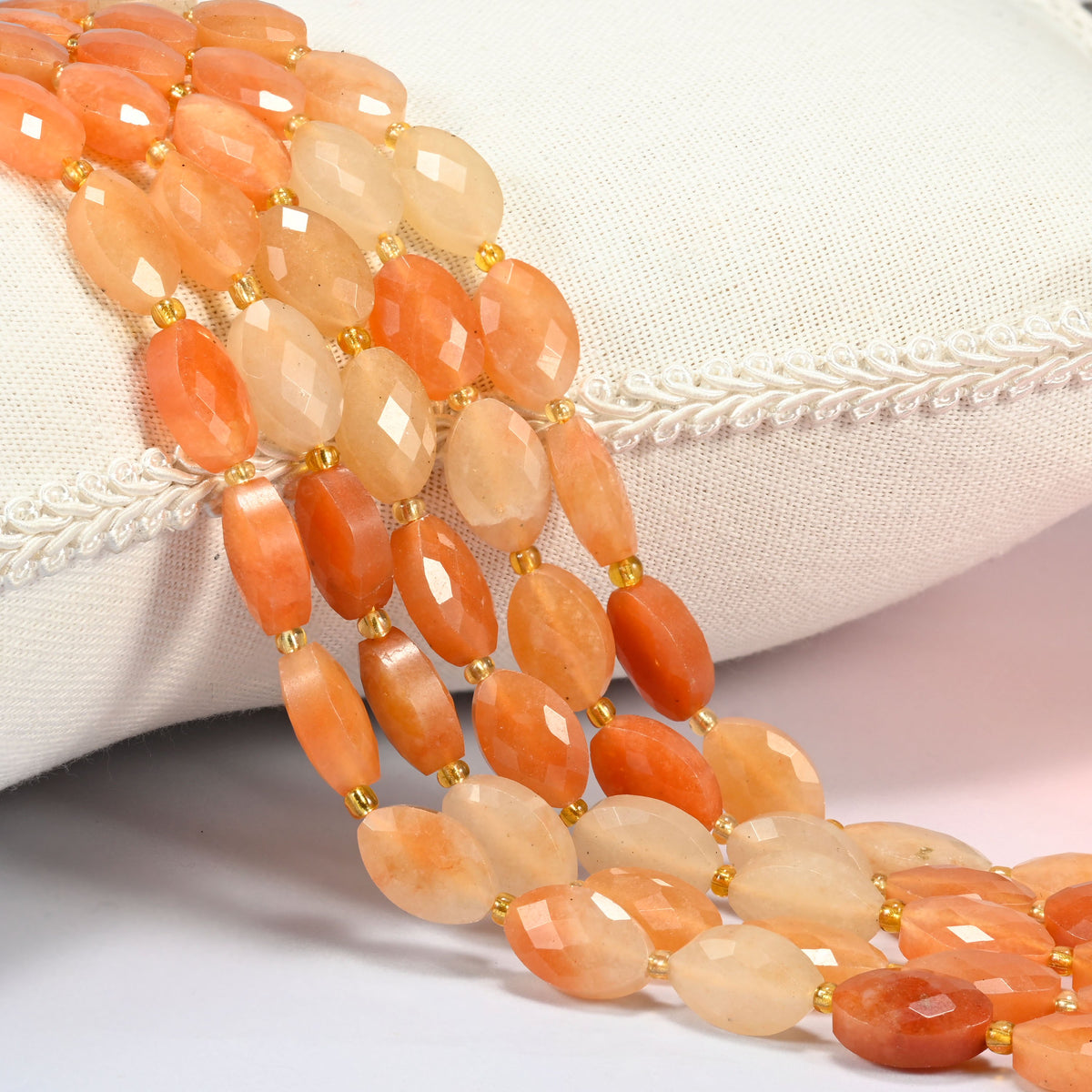 Red aventurine faceted flat oval beads 9x14mm with small gold seed bead spacers, several strands draped over a white cushion
