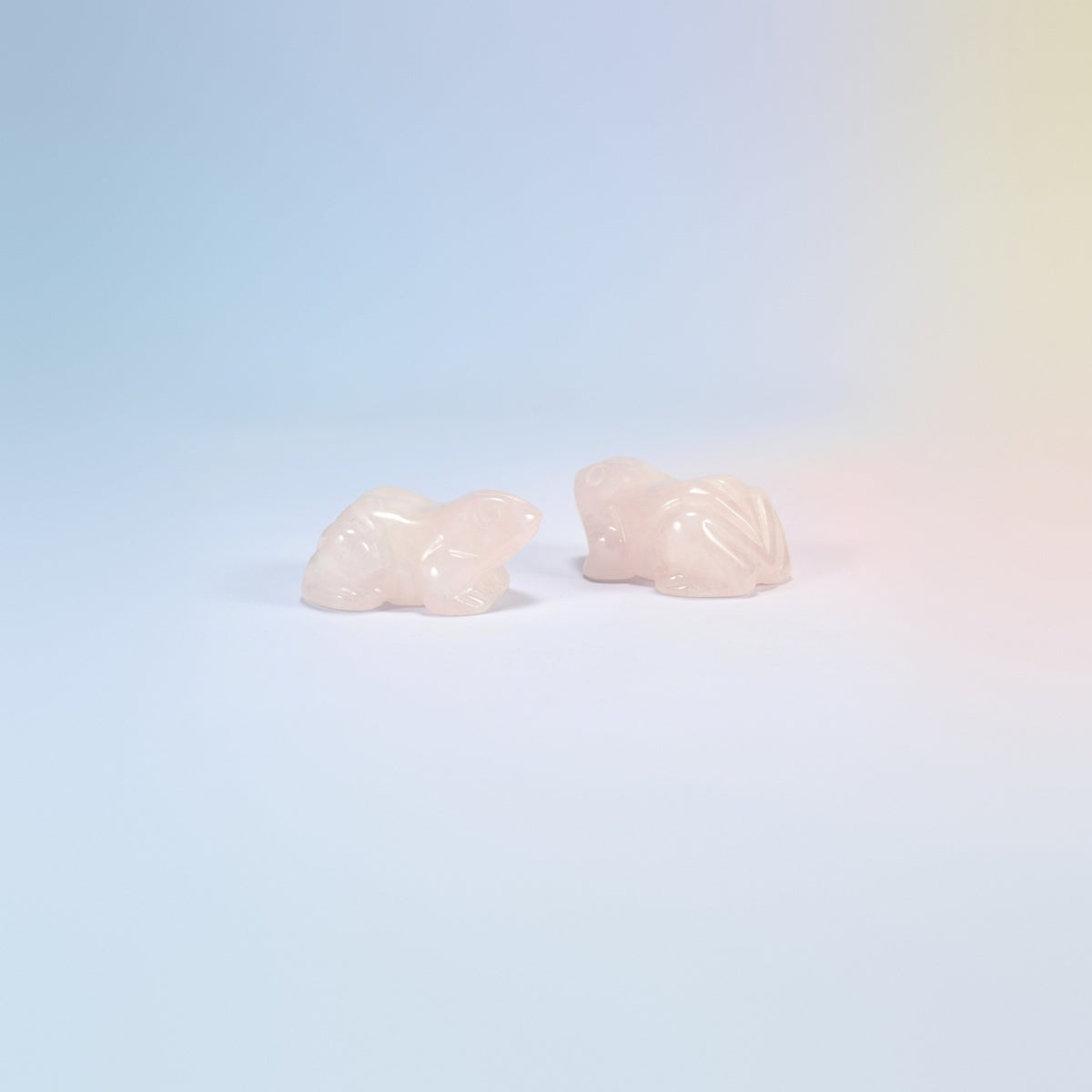 Two natural rose quartz frog carvings, light pink with folded back legs