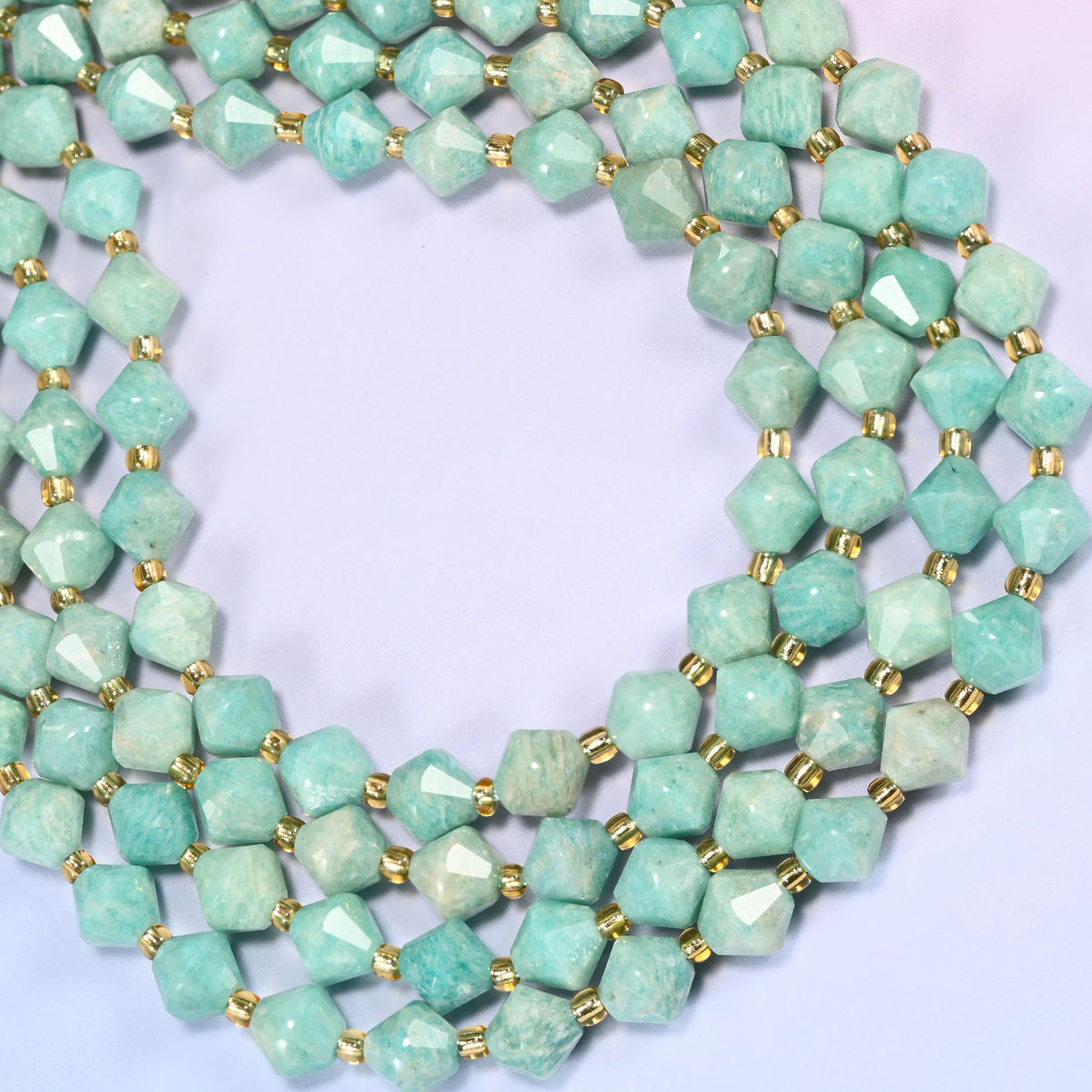 Green Amazonite faceted bicone beads 8mm with gold-tone spacers, strand coiled into a wide circle, close-up of the faceted texture