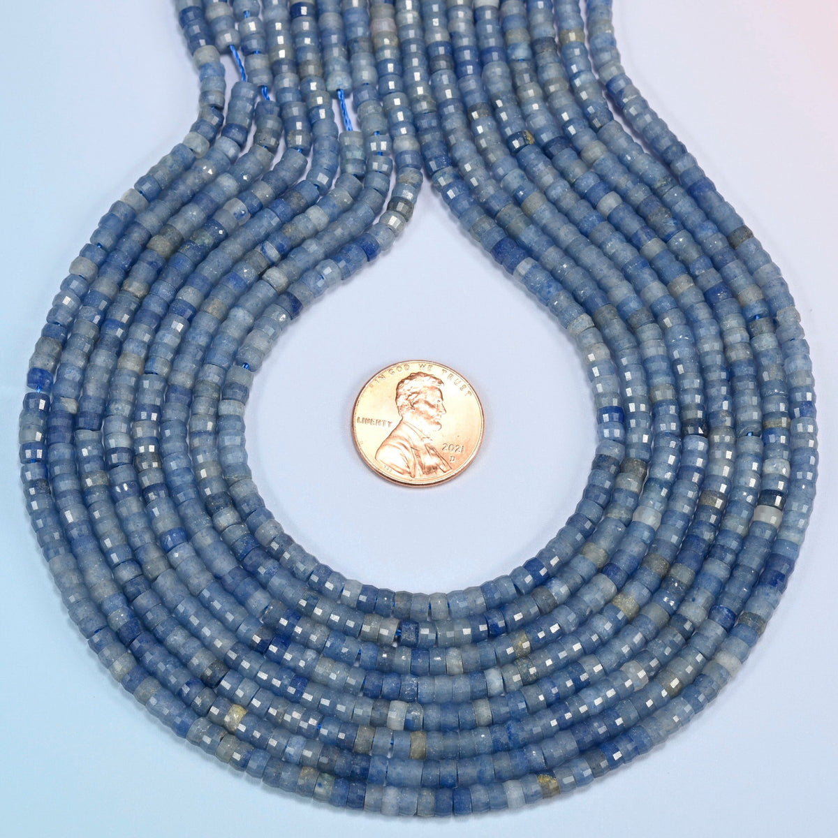 Blue aventurine faceted heishi disc strands formed into a teardrop loop around a US penny for scale