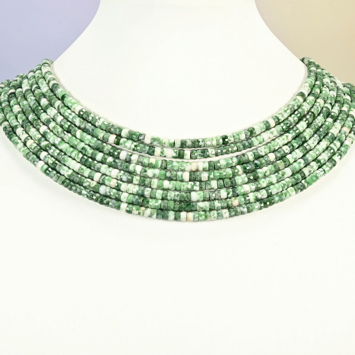 Tree agate faceted heishi disc strands arranged as a layered collar on a white display bust, green and white beads across the neck