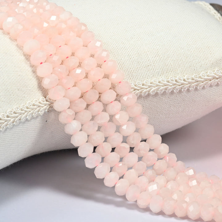 Rose quartz faceted rondelle beads in soft milky pink, three strands draped over a linen cushion