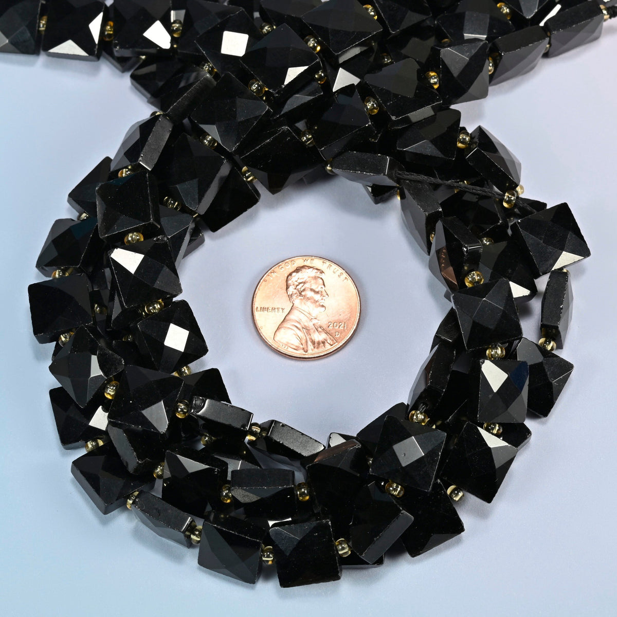 Natural black onyx faceted flat square beads 10x10mm coiled in a loop around a US penny for scale, close-up of the faceted flat square shape