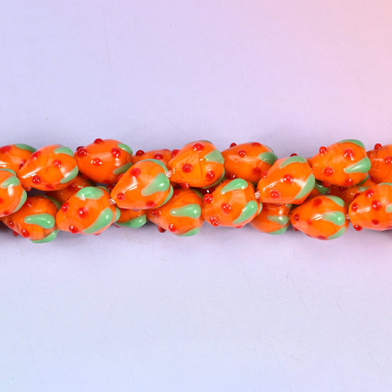 Glossy tangerine orange lampwork strawberries with tiny raised red seed dots and a mint green glass leaf cap