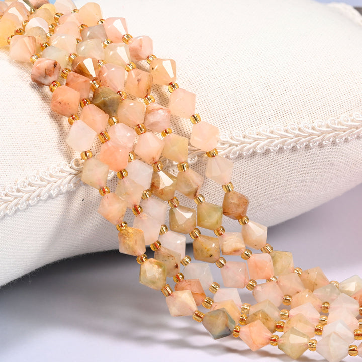 Red Grass Silk Stone faceted bicone beads draped over a cushion, close-up of the fibrous patterning and gold-tone spacers.