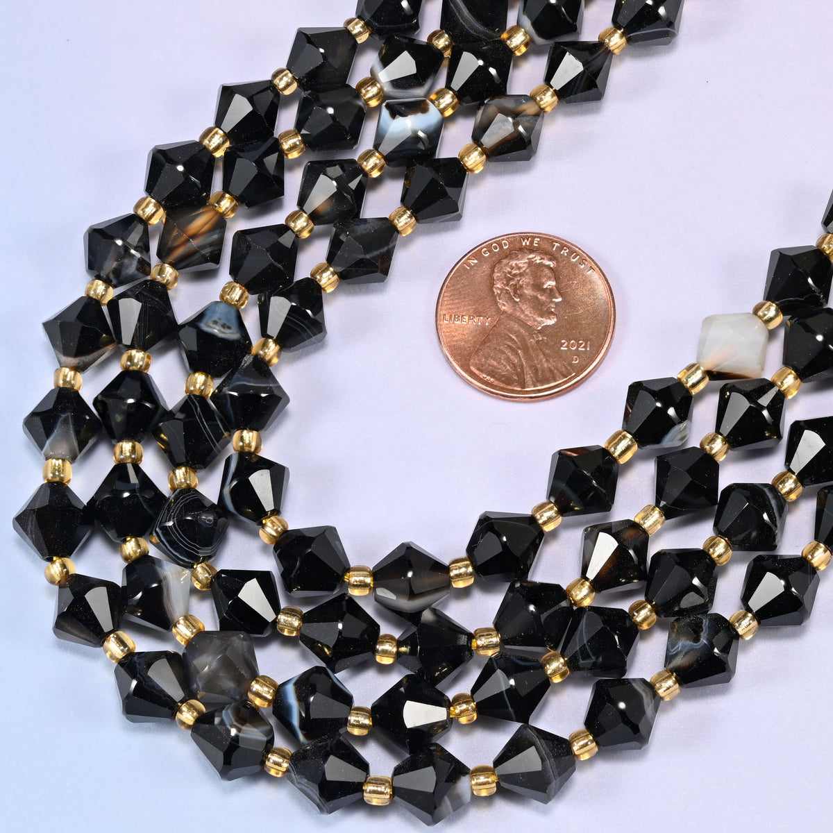 Dyed black strip agate bicone beads in a wide curve, 8mm beads with a gold-tone spacer between each one.