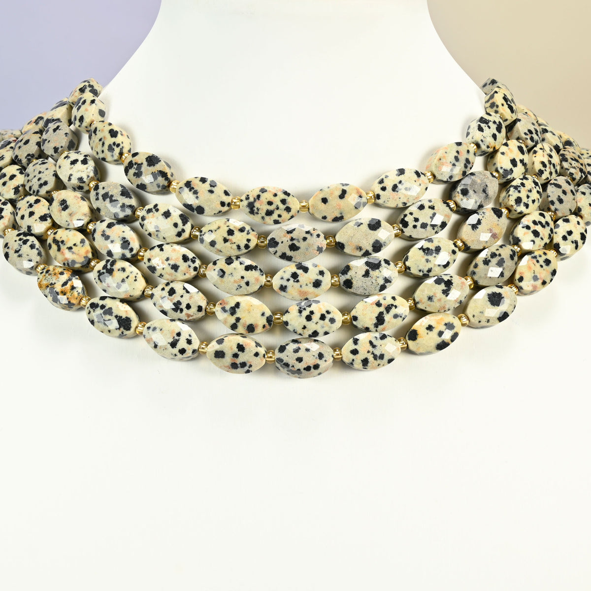 Dalmatian jasper faceted flat oval strands arranged as a layered collar on a white display bust, spotted cream beads across the neck