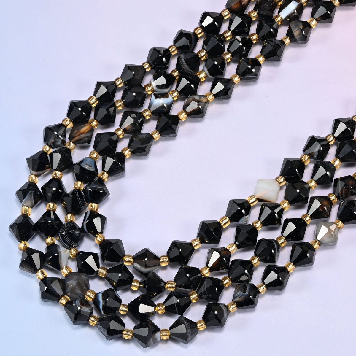 Dyed black strip agate bicone beads in a wide loop curving down and back, banding running at a different angle on every bead.