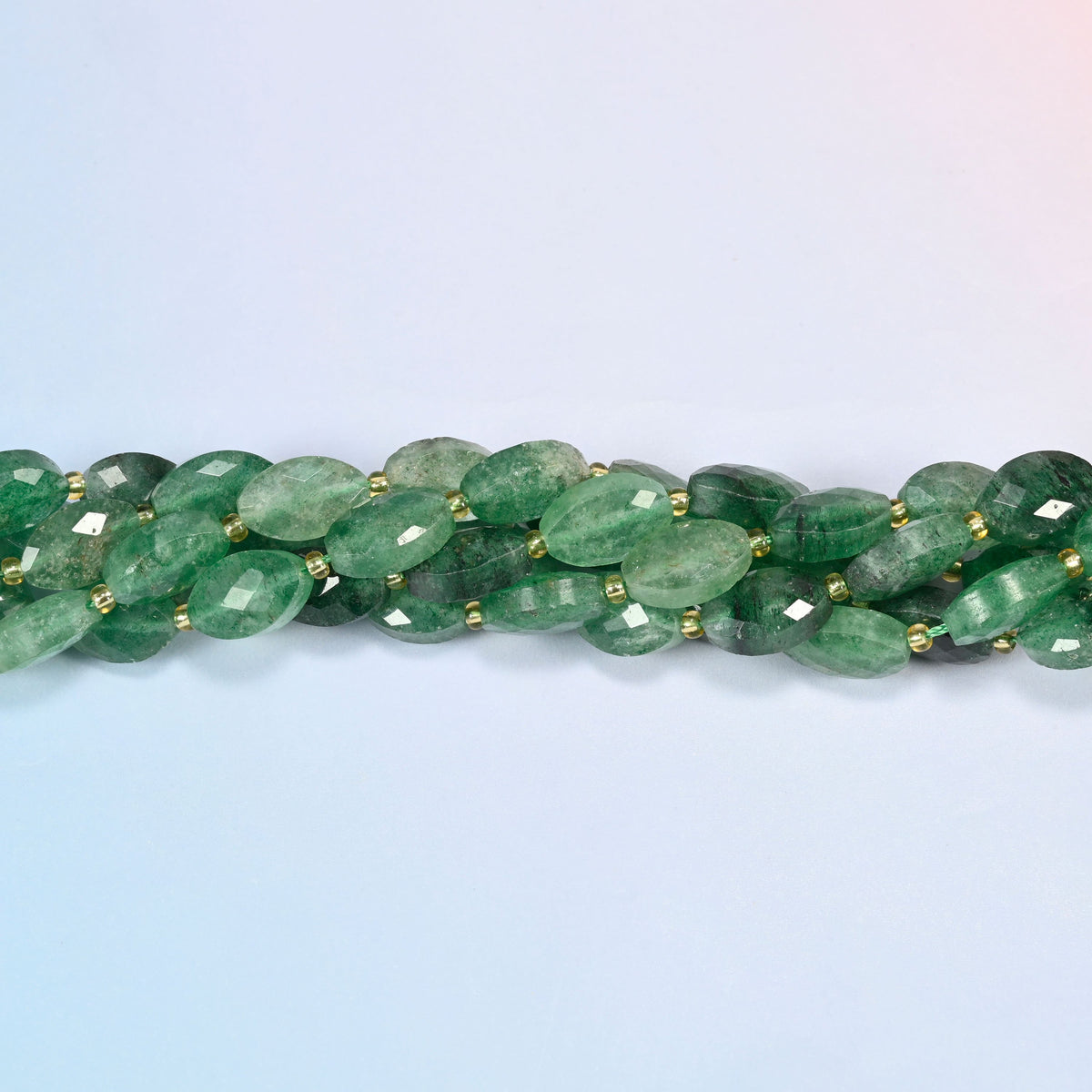 Strands of green strawberry quartz faceted flat oval beads twisted together in a horizontal row
