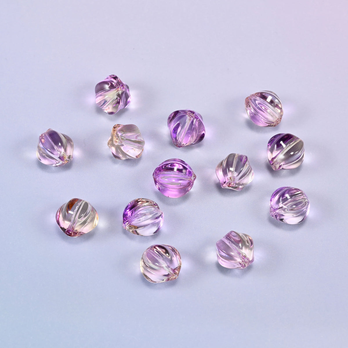 A scattered group of loose 8mm clear purple gold pumpkin glass beads, showing the melon ribs and the drill holes.
