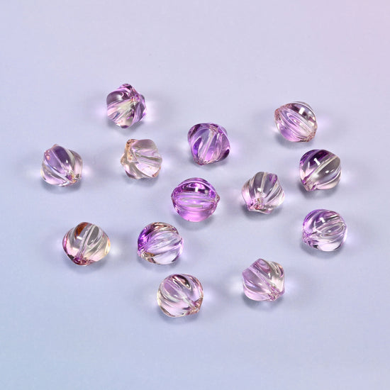 A scattered group of loose 8mm clear purple gold pumpkin glass beads, showing the melon ribs and the drill holes.
