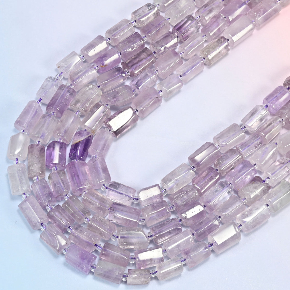Lavender amethyst faceted tube strands sweeping into a wide U fold, milky lilac tubes with a few deeper violet beads.