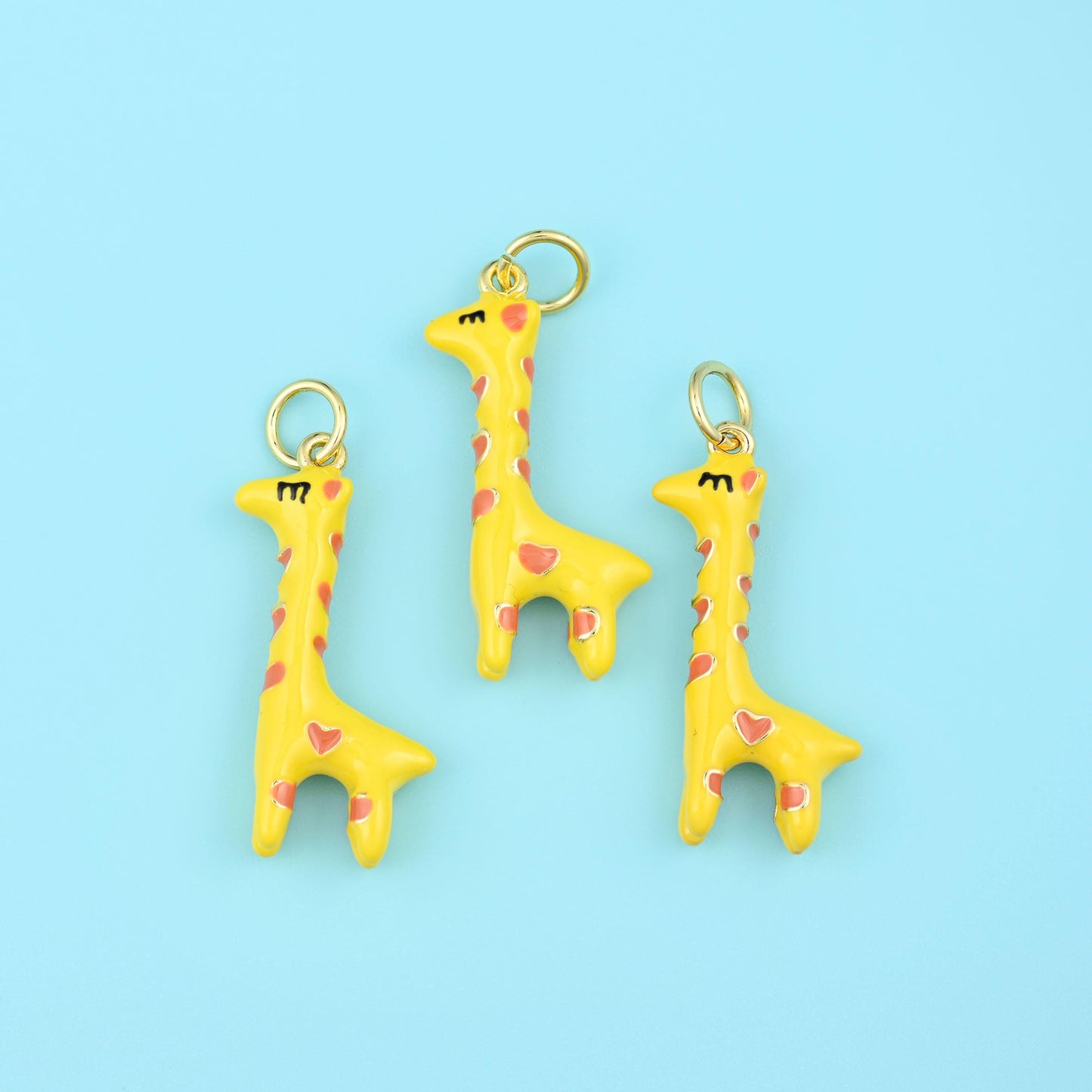 A long-necked giraffe in soft butter yellow enamel, its markings picked out as small pink hearts and its mane and eyelashes…