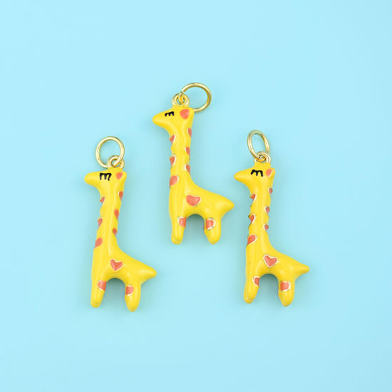 A long-necked giraffe in soft butter yellow enamel, its markings picked out as small pink hearts and its mane and eyelashes…