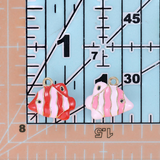 Enamel tropical fish charms in red and pink on a quilting ruler for size comparison.