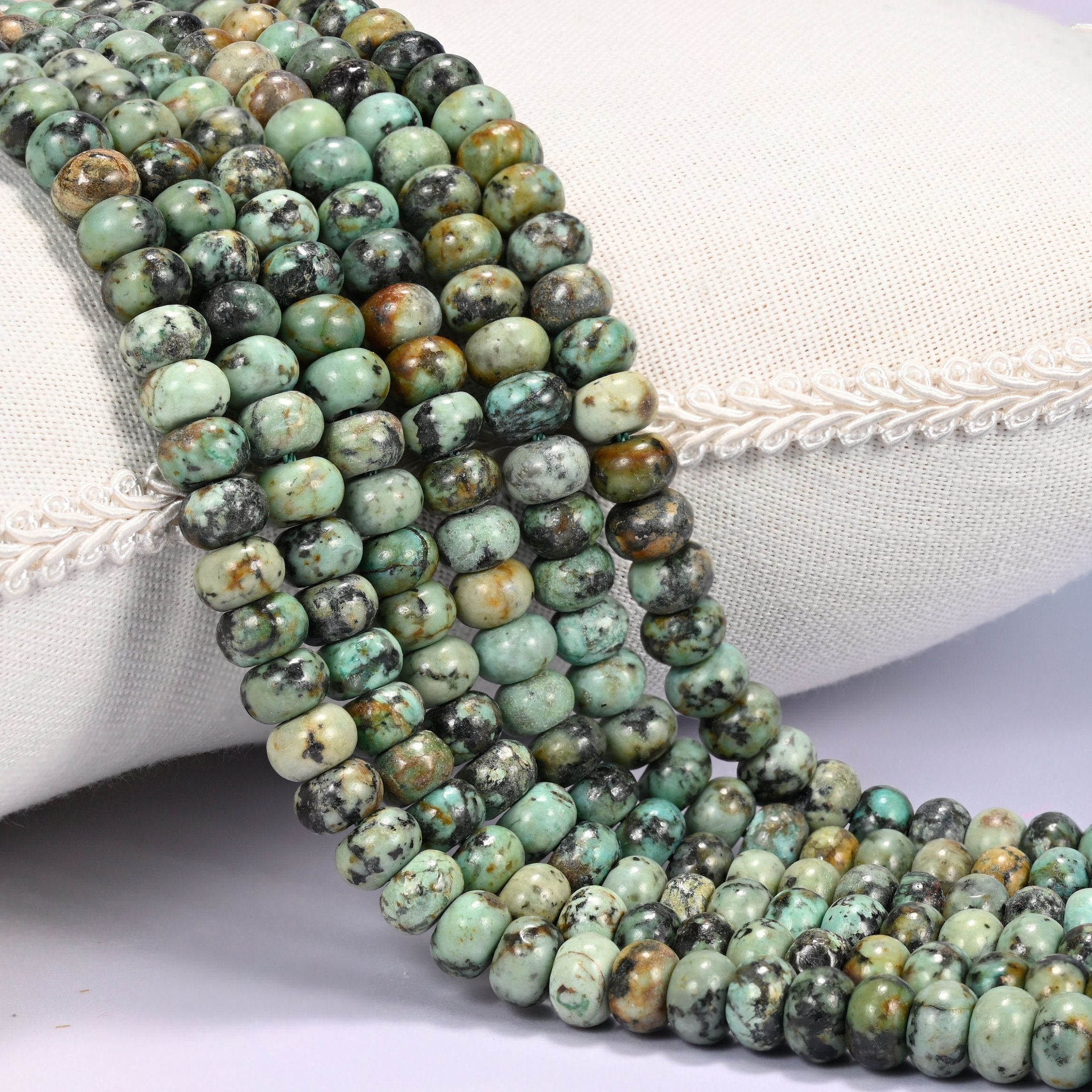 Close-up of multiple strands of polished African Howlite rondelle beads in green and brown-black tones, draped over a cream fabric jewelry display bust.