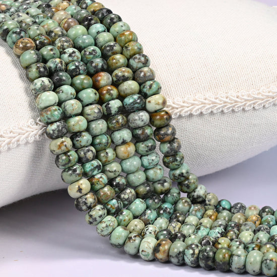 Close-up of multiple strands of polished African Howlite rondelle beads in green and brown-black tones, draped over a cream fabric jewelry display bust.