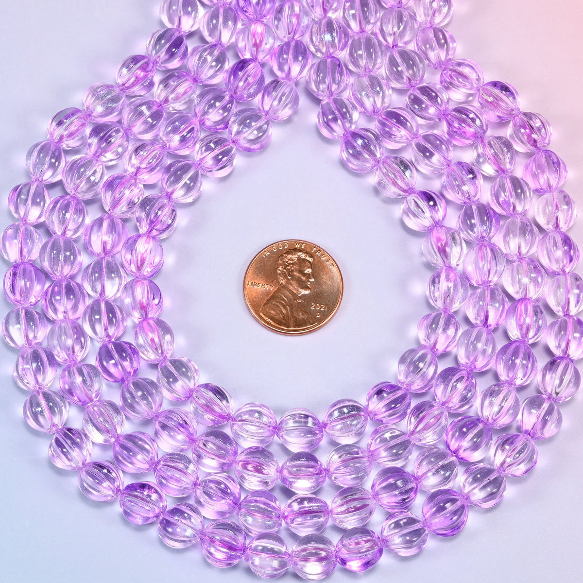 Clear purple pumpkin glass beads coiled into a ring, shown with a US penny in the open center for scale.