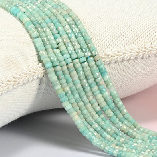 Green amazonite faceted heishi disc beads 2x4mm, several strands draped over a white cushion