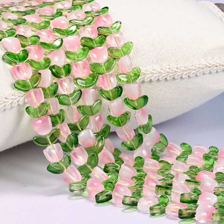 Close-up of pink tulip flower and green leaf glass beads cascading diagonally over a cream woven pillow with decorative trim.