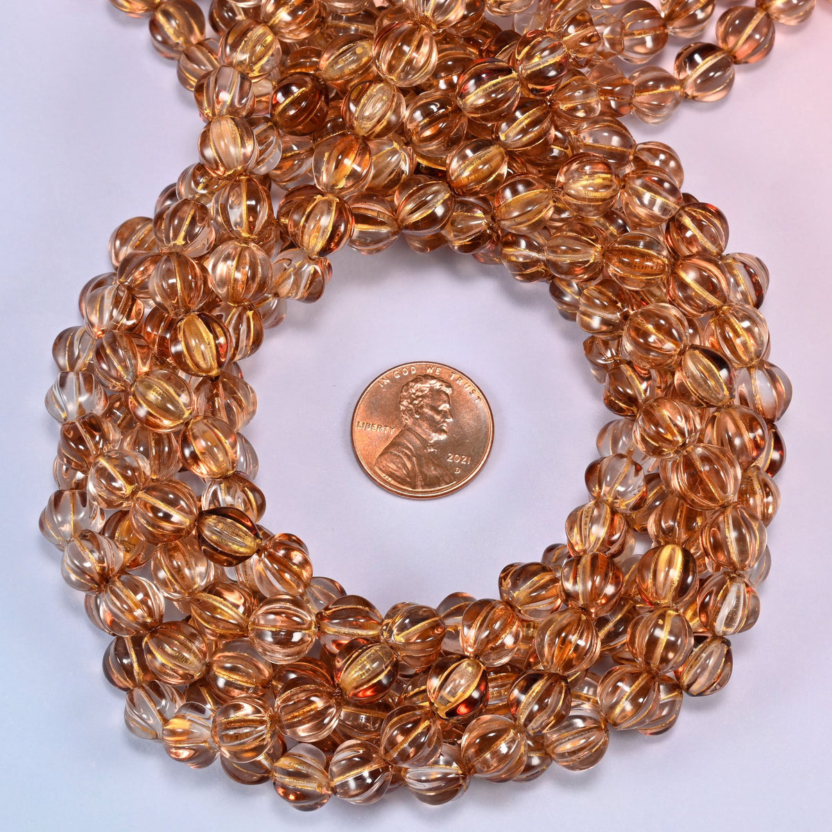 Brown pumpkin glass beads coiled tightly, shown with a US penny in the open center for scale.