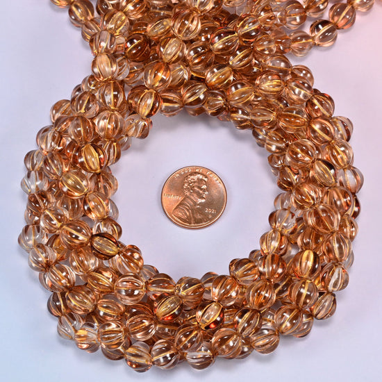 Brown pumpkin glass beads coiled tightly, shown with a US penny in the open center for scale.