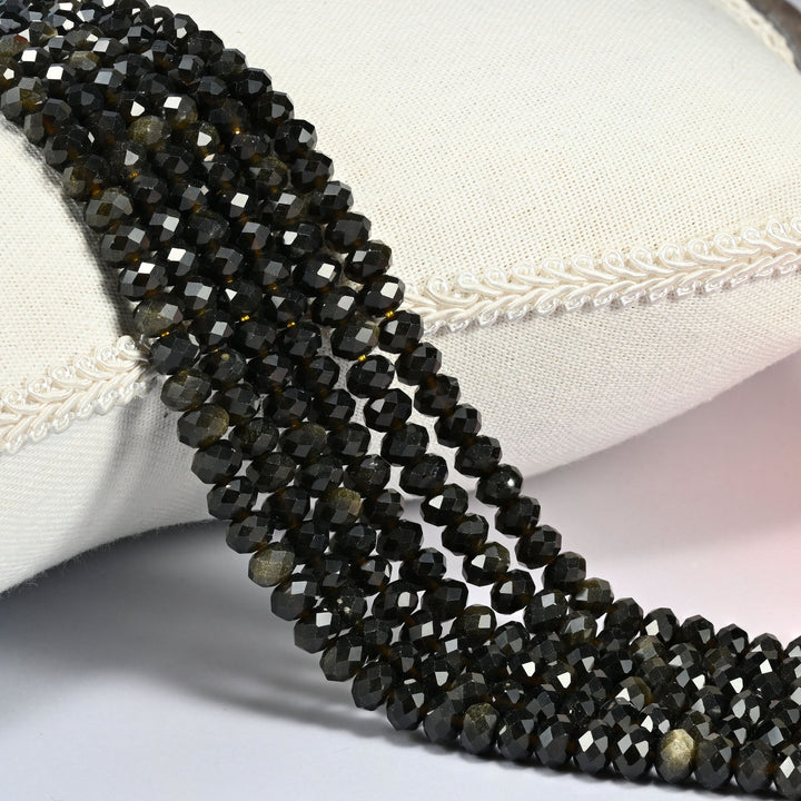 Gold Obsidian gemstone rondelle beads 4x6mm faceted, strand draped over a cream fabric cushion