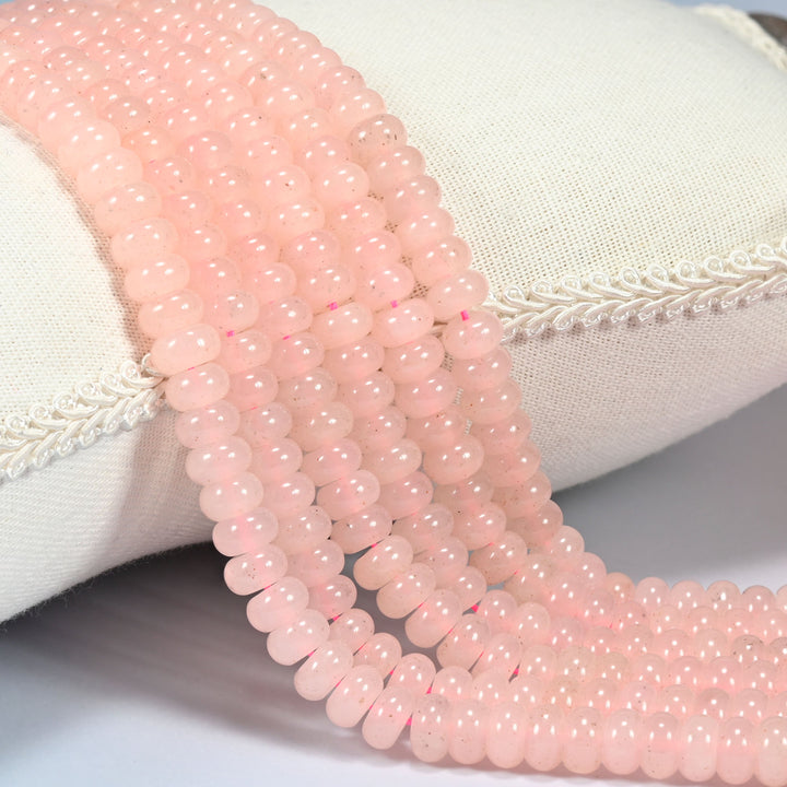 Rose Quartz Color dyed jade gemstone rondelle beads draped over a cushion in soft rows, a soft warm pink, the color of rose quartz
