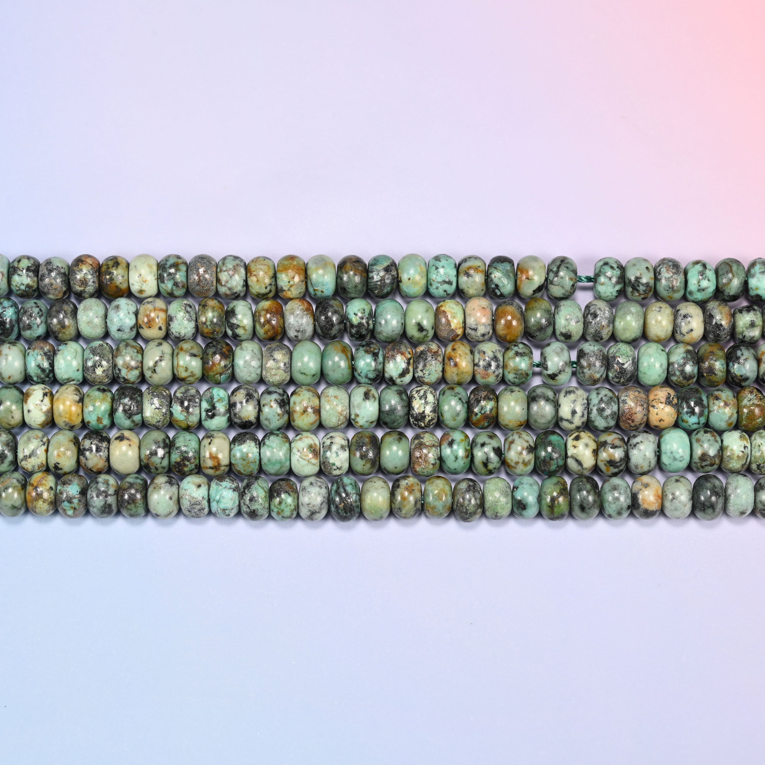 Overhead view of several rows of African Howlite rondelle beads showing the green and dark matrix coloring on a light lavender surface.