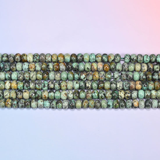 Overhead view of several rows of African Howlite rondelle beads showing the green and dark matrix coloring on a light lavender surface.