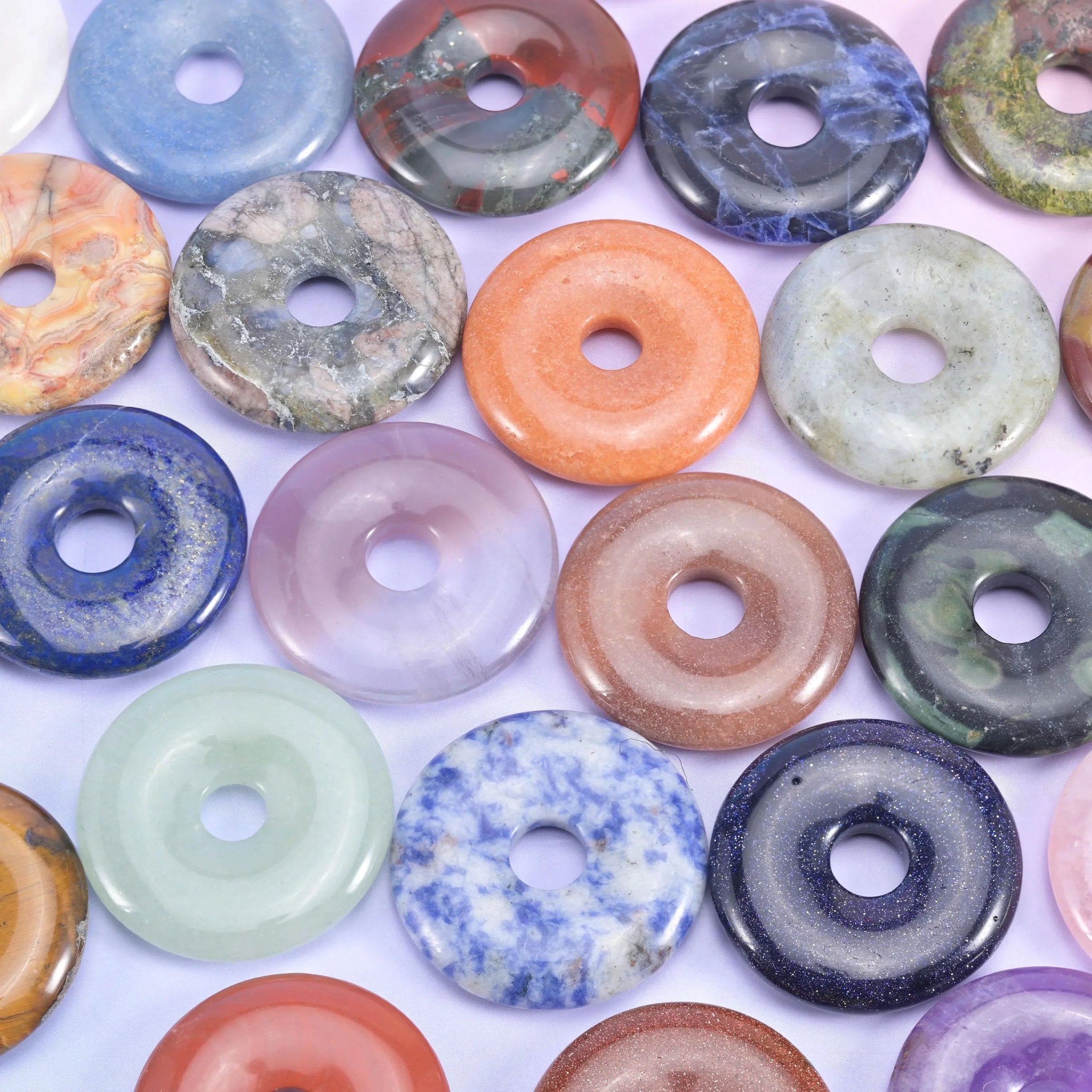 Close pile of 30mm stone donuts in mixed colours, from lapis blue and rose quartz to orange jasper