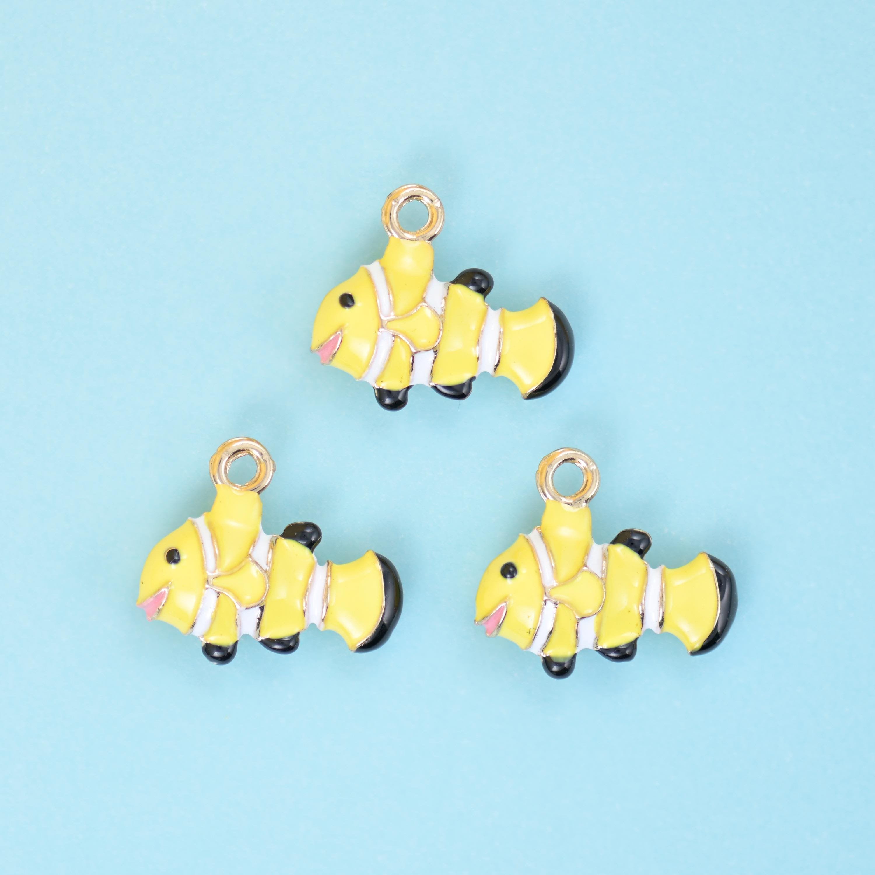 A chubby little clown fish in buttercup yellow enamel with white banding, black-tipped fins and a small pink mouth,…