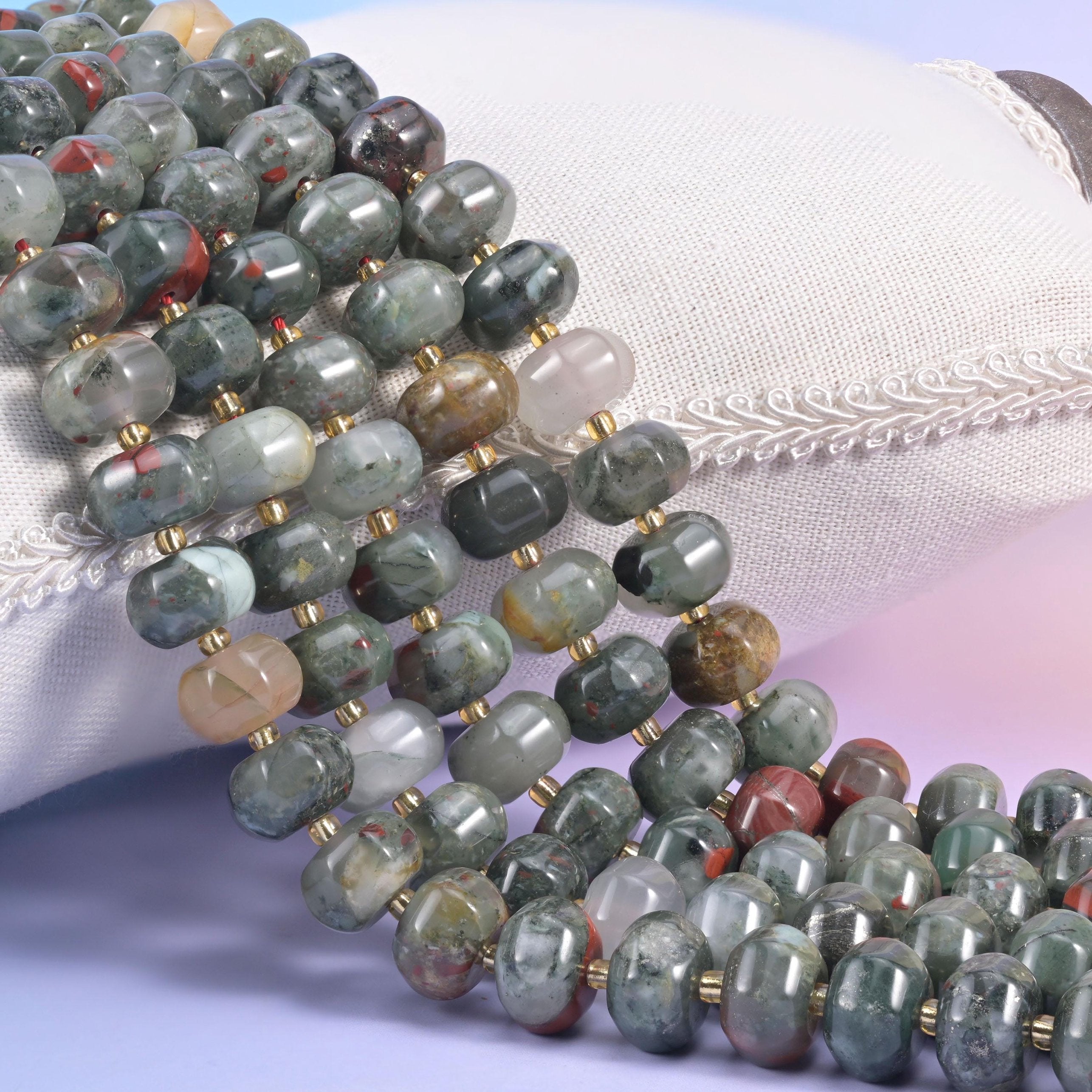 African bloodstone pumpkin rondelle strands on a cream cushion, ribbed grey-green beads with gold spacers