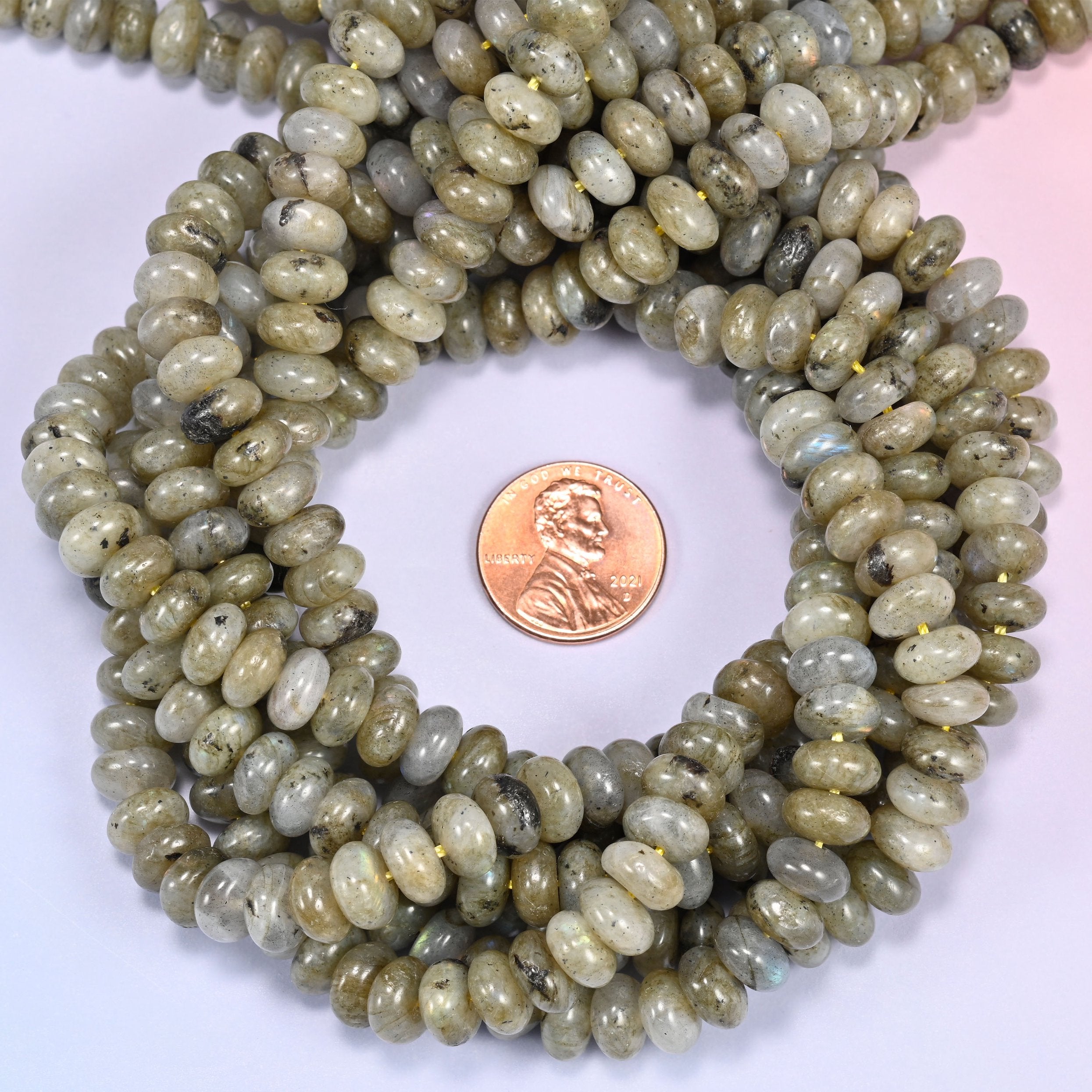 Close-up of individual loose Grey Labradorite beads laid out on a white surface, showing the large center-drilled hole and creamy grey coloring of each bead.