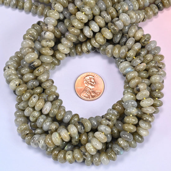 Close-up of individual loose Grey Labradorite beads laid out on a white surface, showing the large center-drilled hole and creamy grey coloring of each bead.