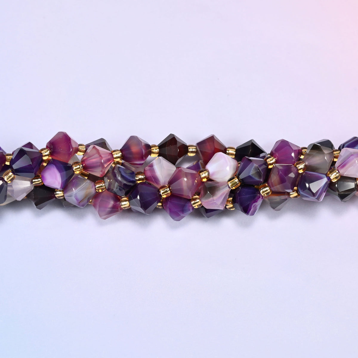 Macro close-up of 8mm Dyed Purple Strip Agate faceted bicone beads on a strand, showing the faceted cut and gold-tone spacer beads.