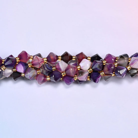 Macro close-up of 8mm Dyed Purple Strip Agate faceted bicone beads on a strand, showing the faceted cut and gold-tone spacer beads.