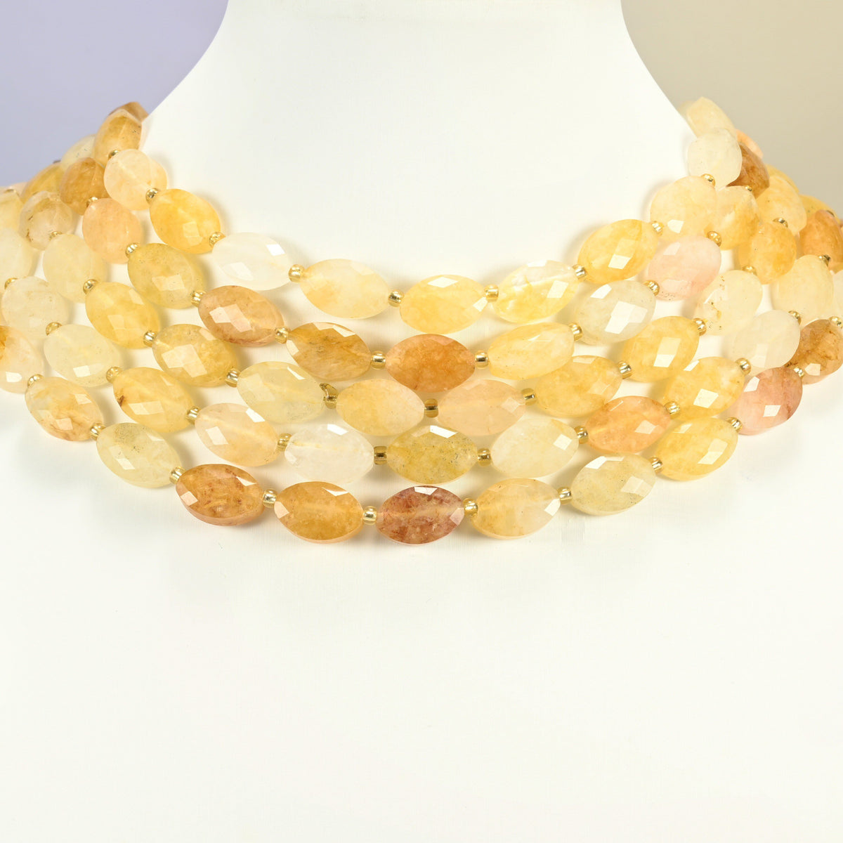 Golden healer quartz faceted flat oval strands arranged as a layered collar on a white display bust, golden yellow beads across the neck
