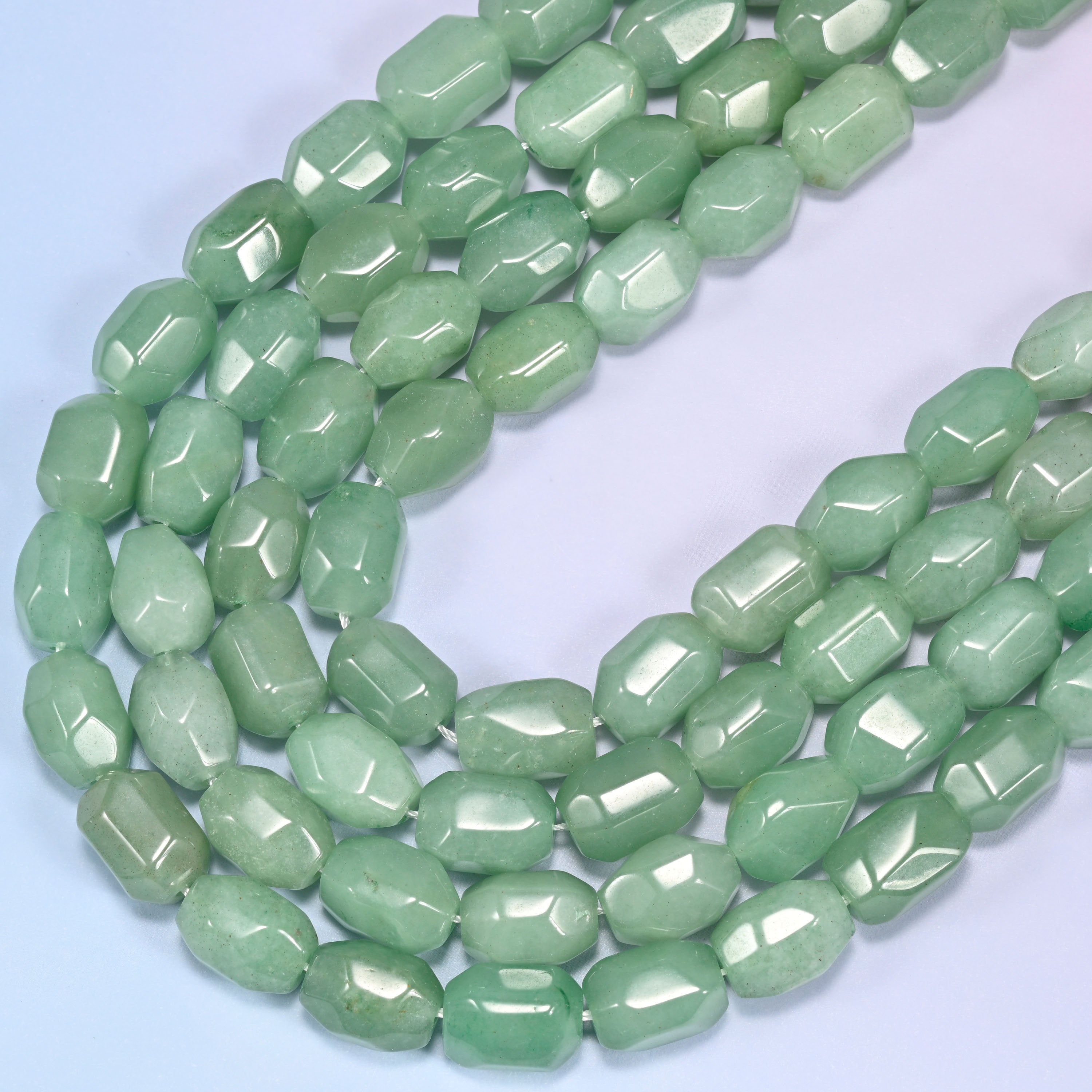 Close-up of a circular coil of green faceted Aventurine barrel beads on a light lavender background.