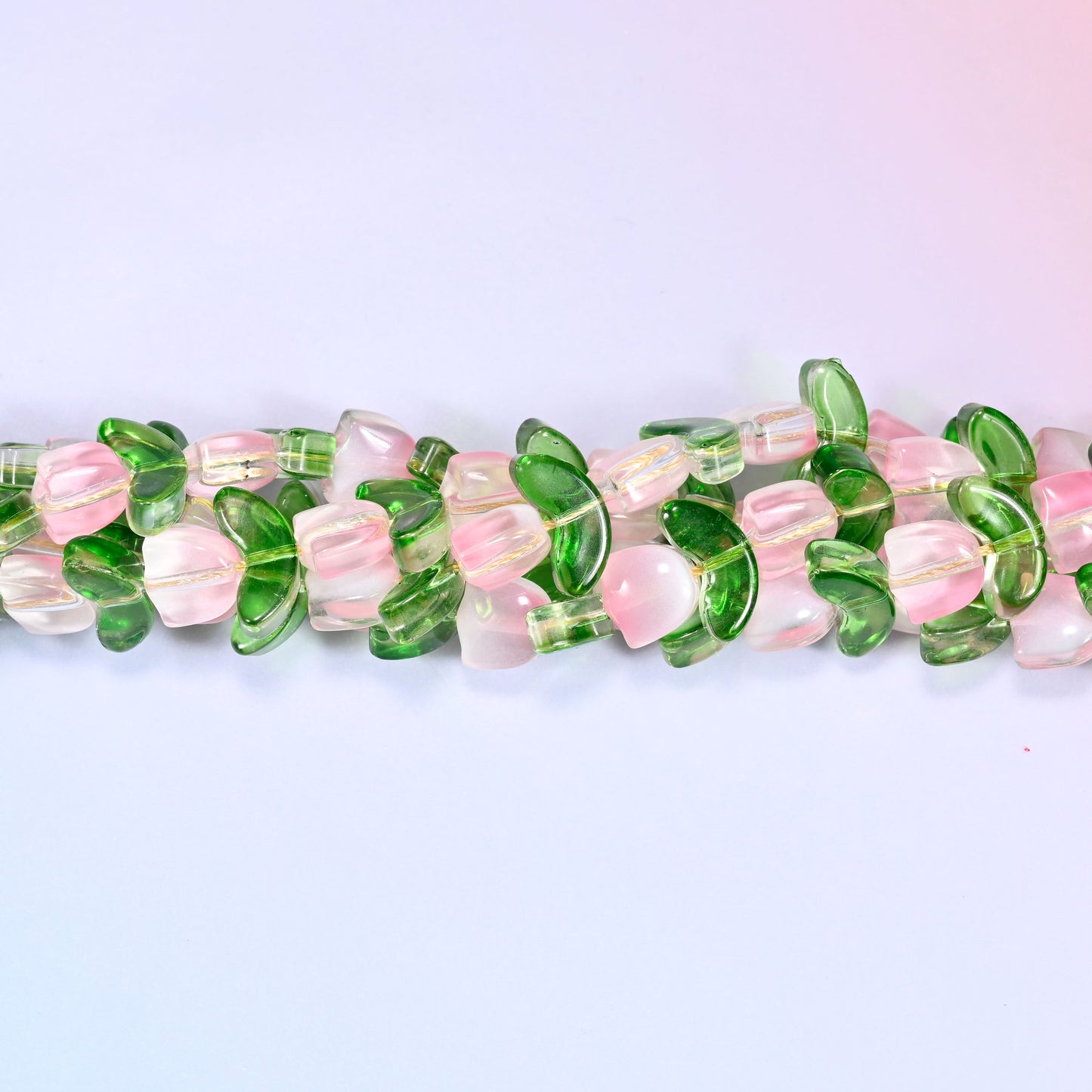 Horizontal row of pink tulip and green leaf glass beads laid straight across a lavender and pink gradient background.