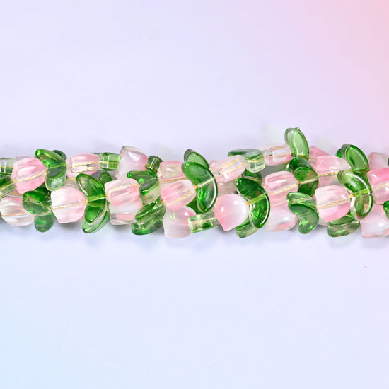 Horizontal row of pink tulip and green leaf glass beads laid straight across a lavender and pink gradient background.