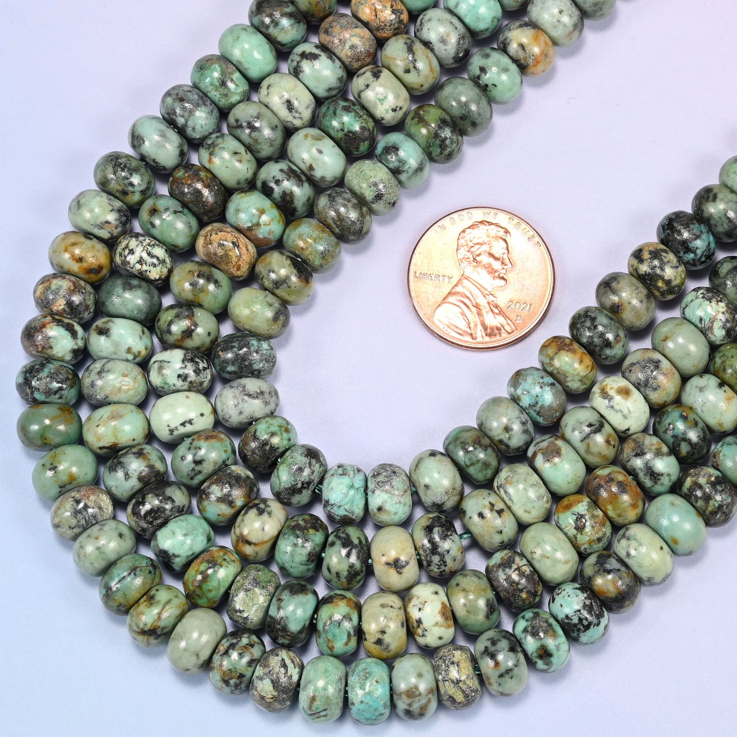Rows of African Howlite rondelle beads laid straight on a lavender surface, showing the natural stone color variation.
