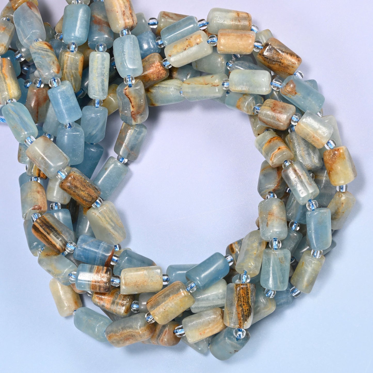 Close-up horizontal row of faceted Blue Calcite tube beads showing the blue and tan banded pattern with clear glass spacer beads.