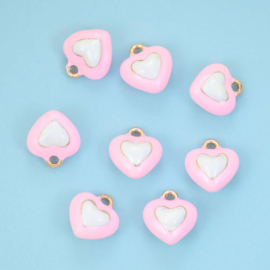 A small heart with a second heart nested inside it, both filled with enamel in contrasting tones and outlined in gold.…