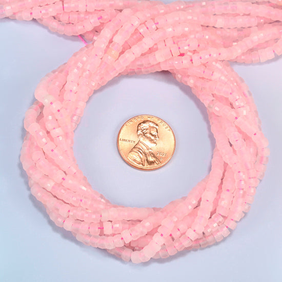 Rose quartz faceted heishi disc beads 2x4mm coiled in a loop around a US penny for scale, close-up of the faceted disc shape